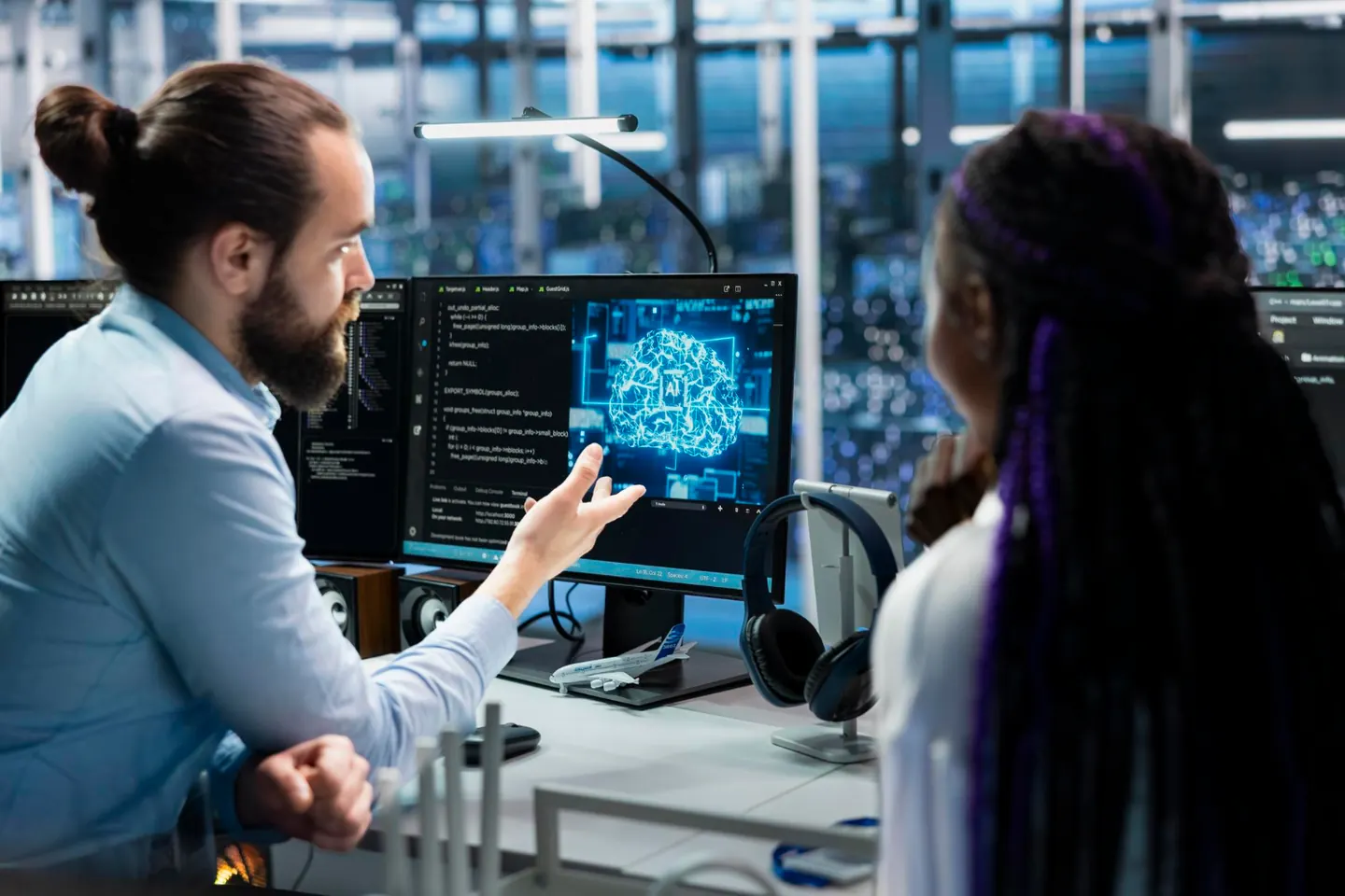 Two people discussing technology at a workstation with AI visualisations